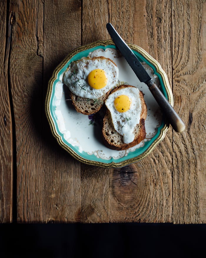 gallery-img-04 From above of appetizing fried eggs on toasts in plate near knife on wooden table
